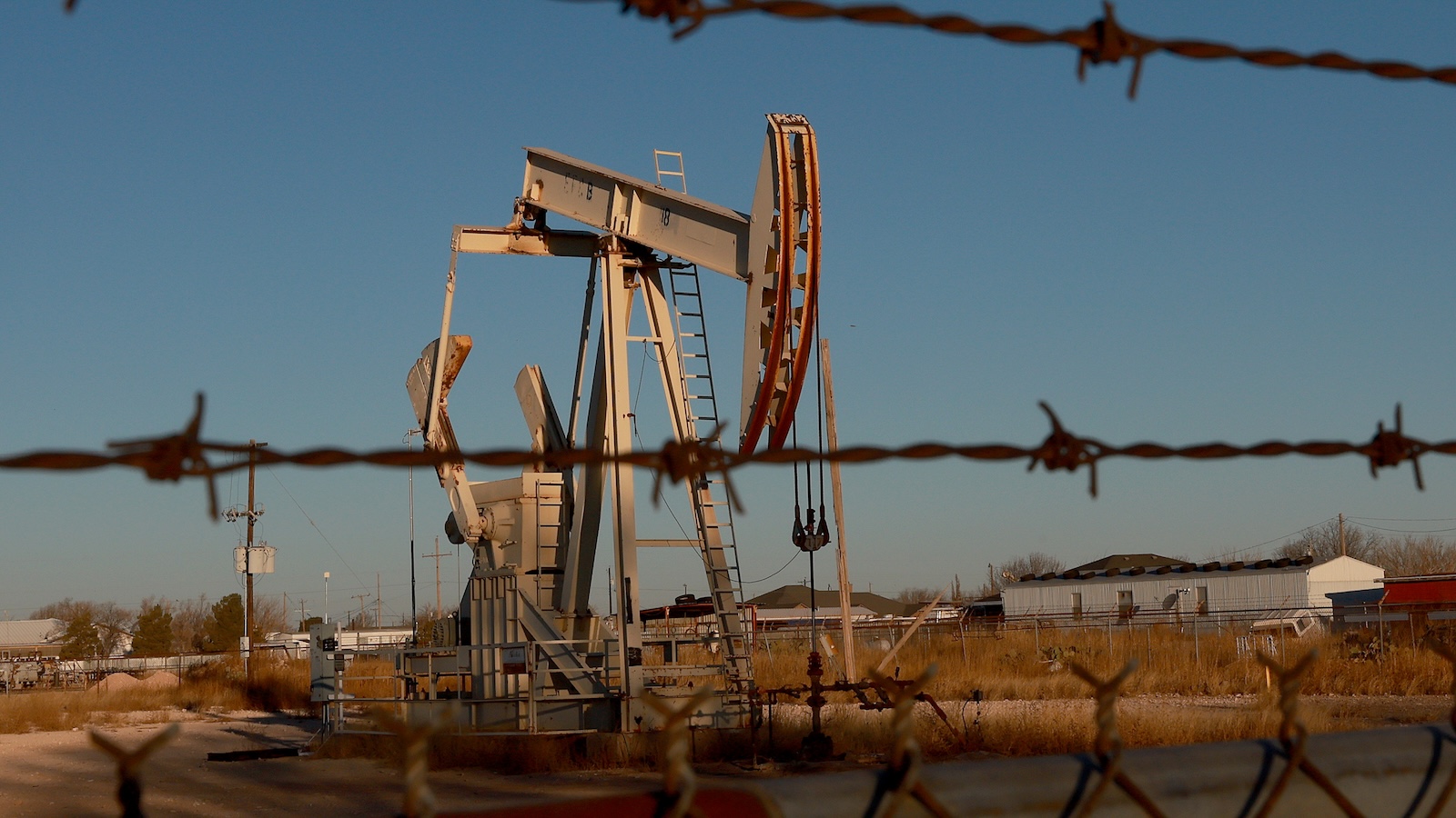 A pumpjack in an oil field, behind barbed wire fence.