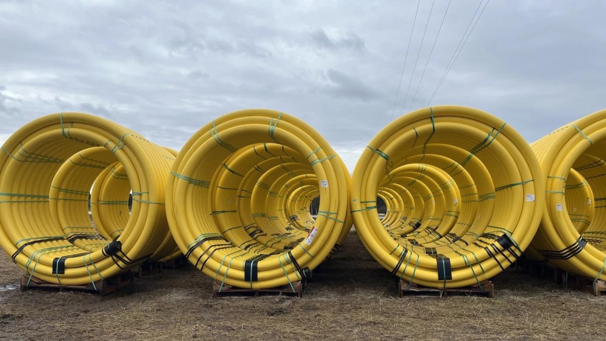 Giant yellow coils of pipeline sit on ground against blue/gray sky.
