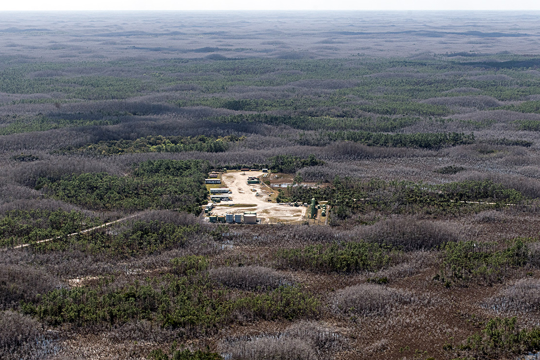 An aerial view of a sand pit with a scattering of small structures in the middle of a green expanse.