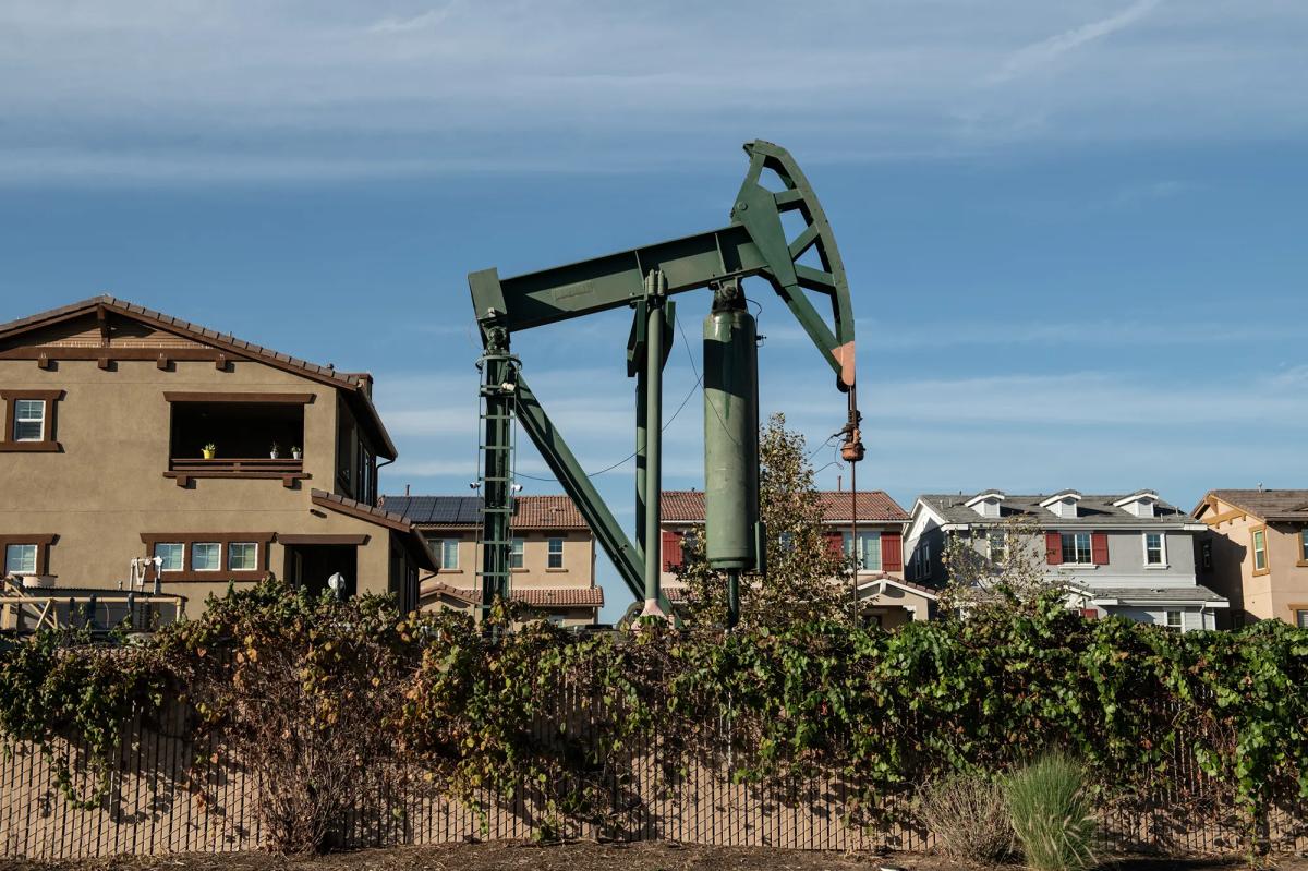 An oil derrick sits next to a home in a residential neighborhood.