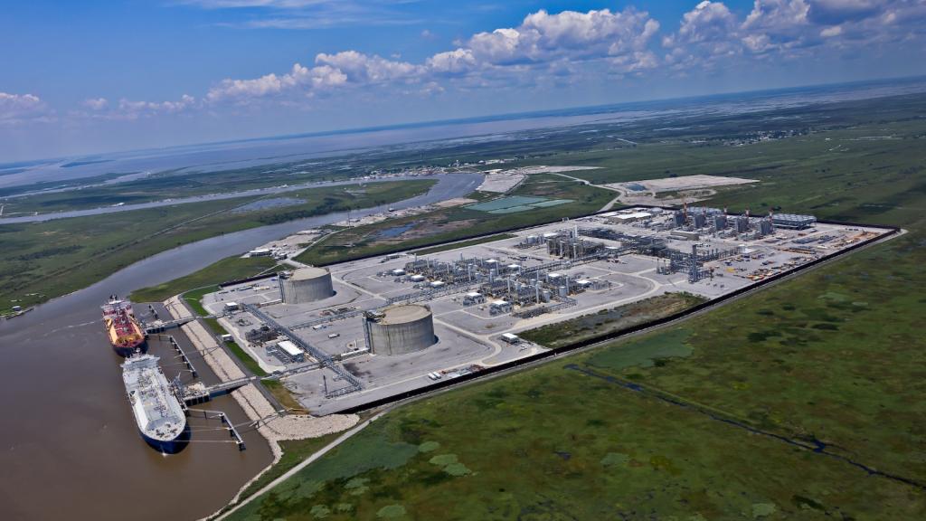 An aerial view of a massive industrial complex on a brown river, surrounded by trees.