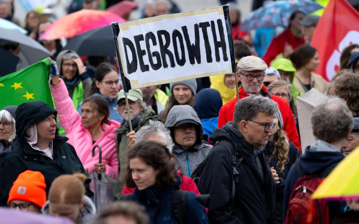 A man holds up a sign reading DEGROWTH amidst a crowd of protesters.