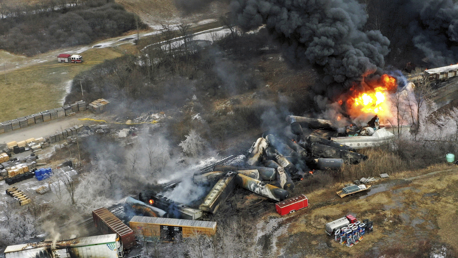 Railroad cars on fire and derailed off track, flung to the sides of the tracks with a ball of fire and lots of dark smoke.