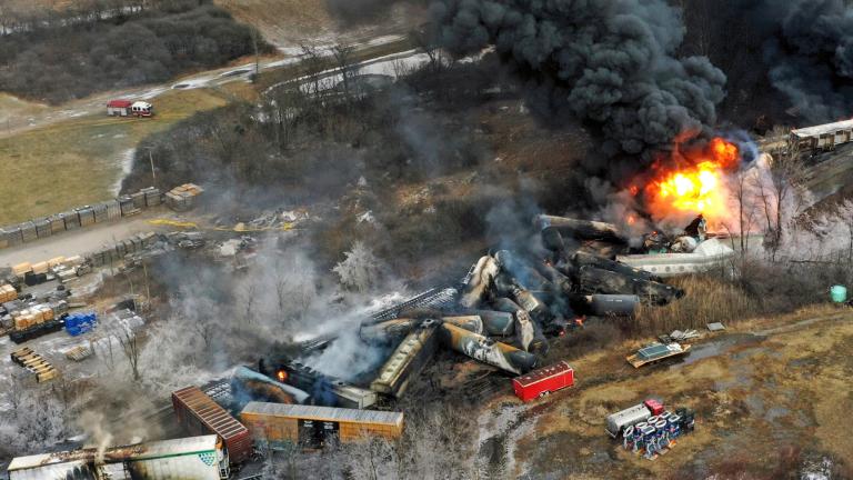 Railroad cars on fire and derailed off track, flung to the sides of the tracks with a ball of fire and lots of dark smoke.