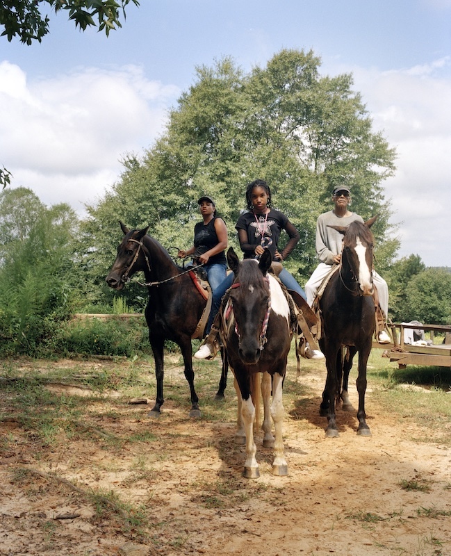Three people sit on horses in front of a large tree