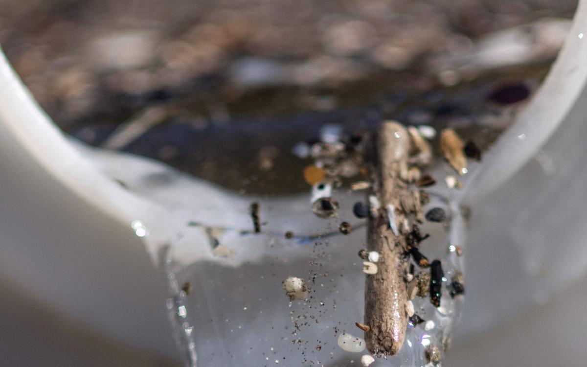 A closeup shot of the mouth of a large container with water spilling out of it, and bits of plastic and sand visible in the stream