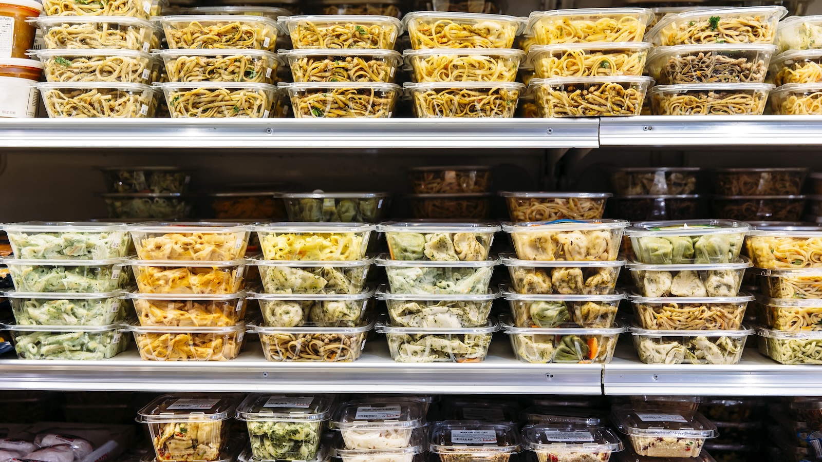 Plastic containers of prepared salad are stocked on three grocery store shelves.