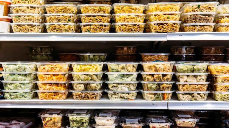 Plastic containers of prepared salad are stocked on three grocery store shelves.