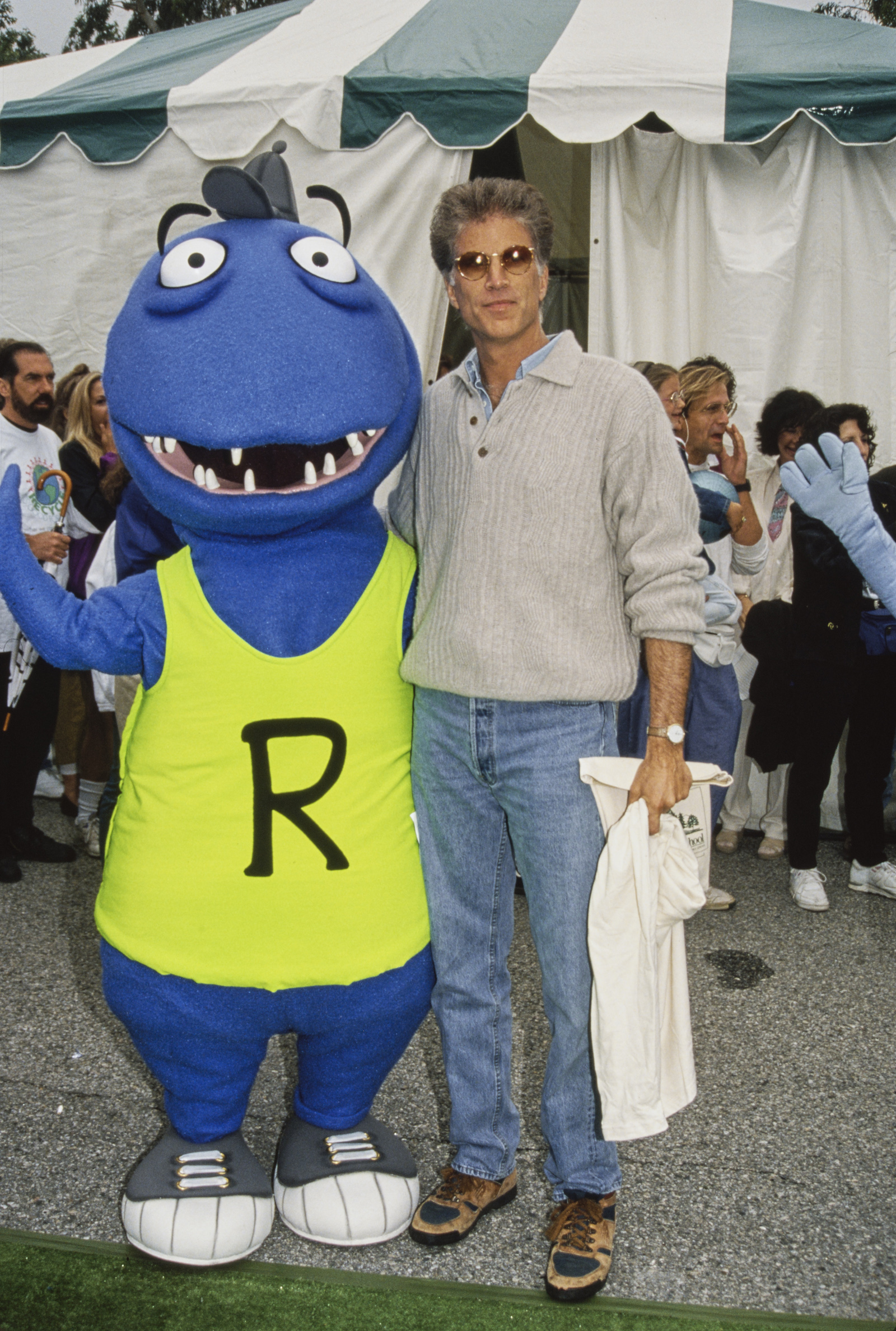 A blue dinosaur mascot with a neon green 'R' shirt next to a tall man in sunglasses