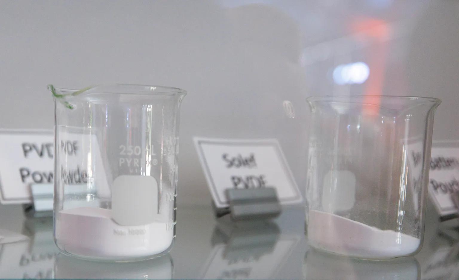 Two beakers sit on a table with white substances in them.
