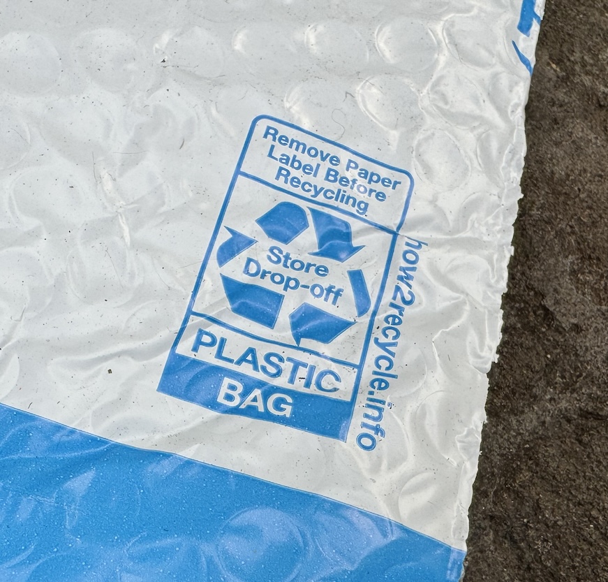Close-up of a recycling symbol on a blue and white Amazon bag. The symbol says "store drop-off" and "plastic bag."
