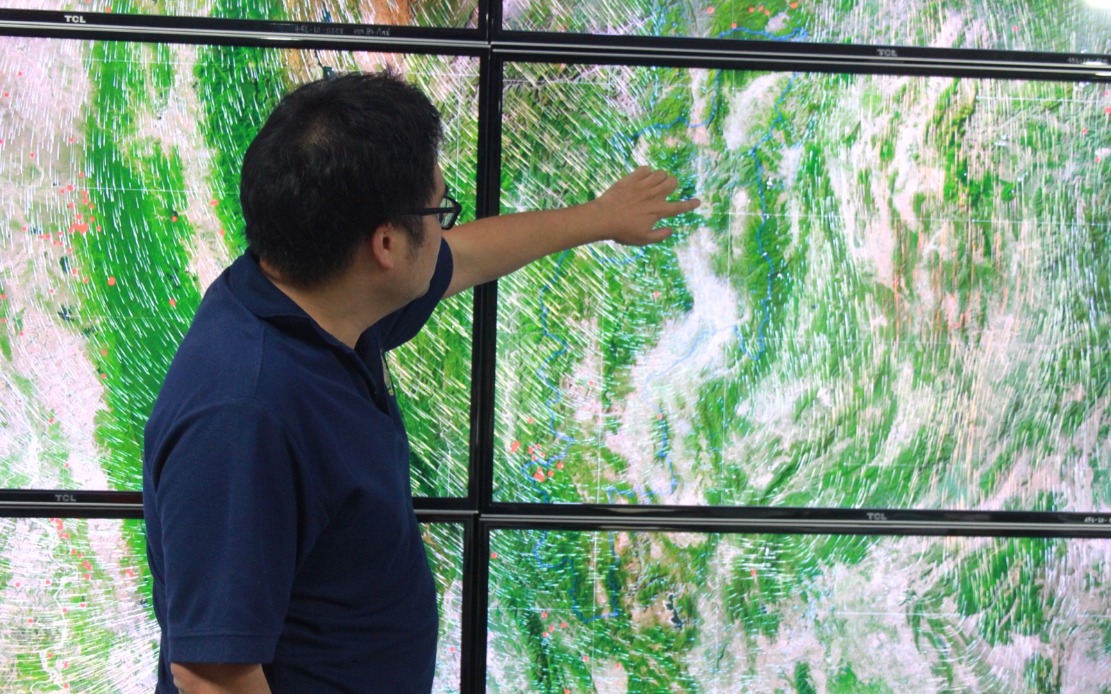A man points to one of several screens showing a topographical map with arrows all over it