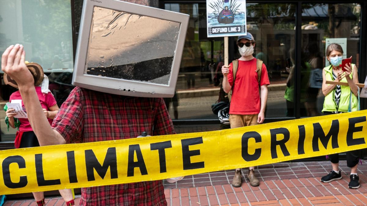 A piece of yellow tape that reads CLIMATE CRIME extends in front of a group of protestors.