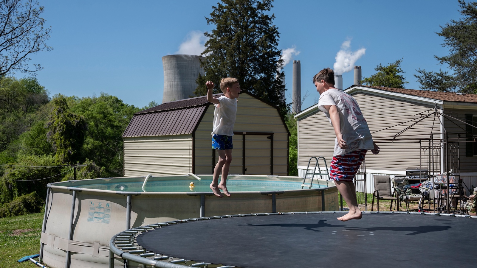 Children play on a trampoline outside their grandparents' home as steam rises from the James H. Miller Jr. coal-fired power plant in Adamsville, Alabama.