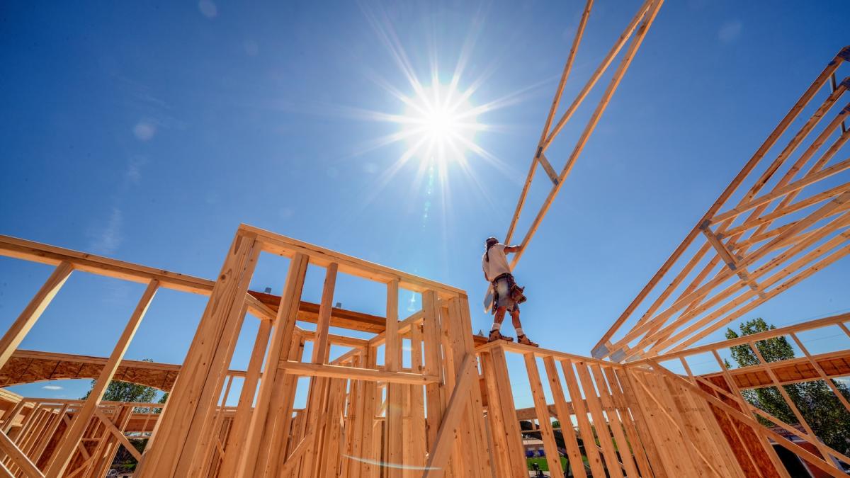 A carpenter framing a house positions a truss while assembling the roof.