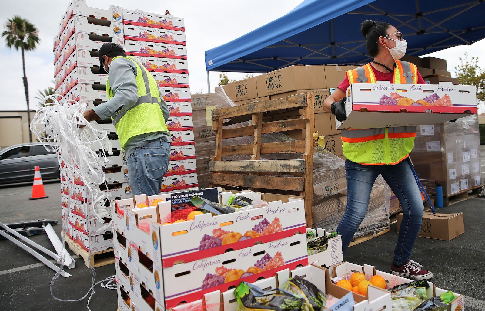 two workers in neon vest move boxes of food from a large stack
