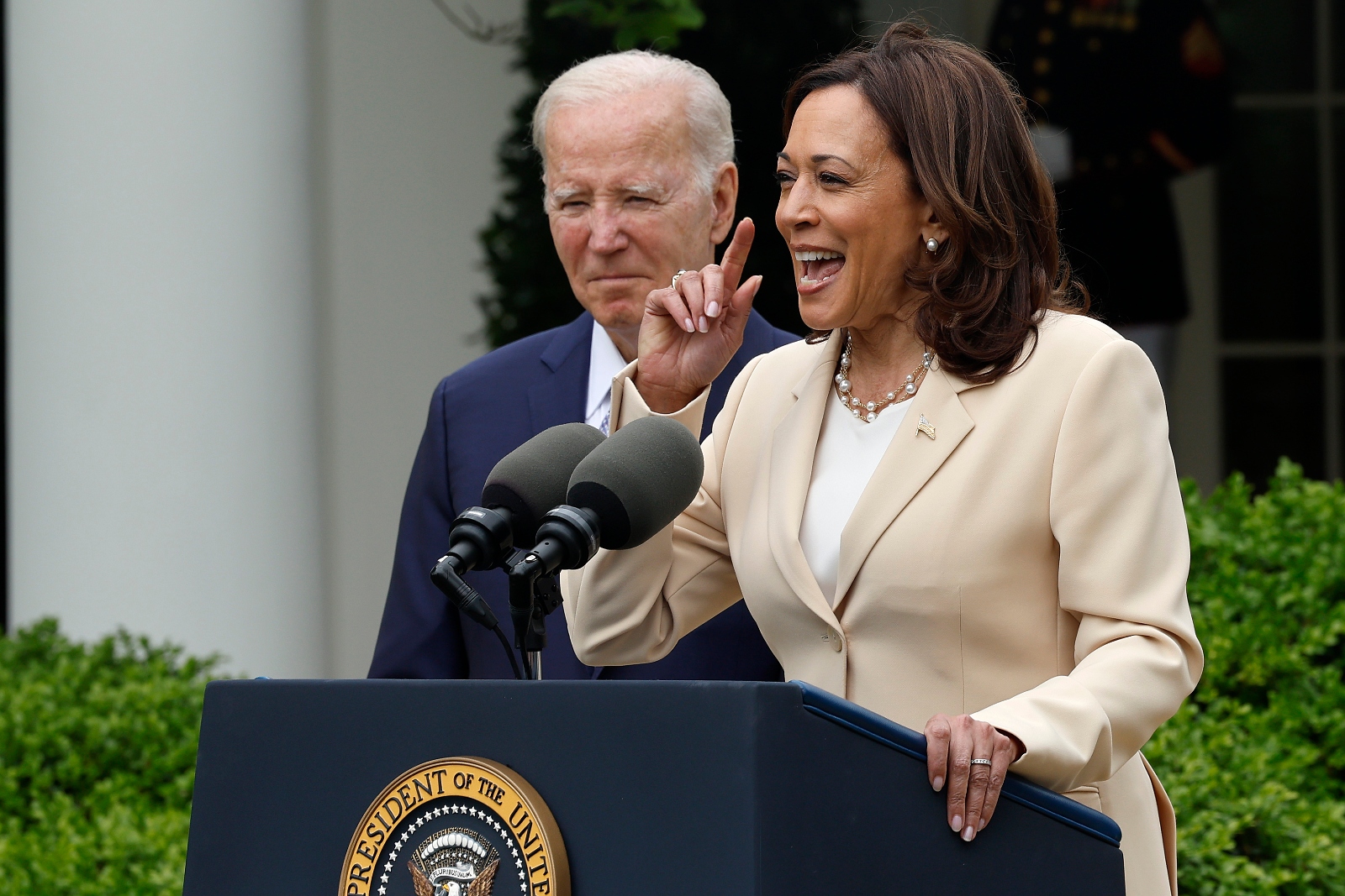 Kamala Harris speaks at a lectern outside with Joe Biden in the background