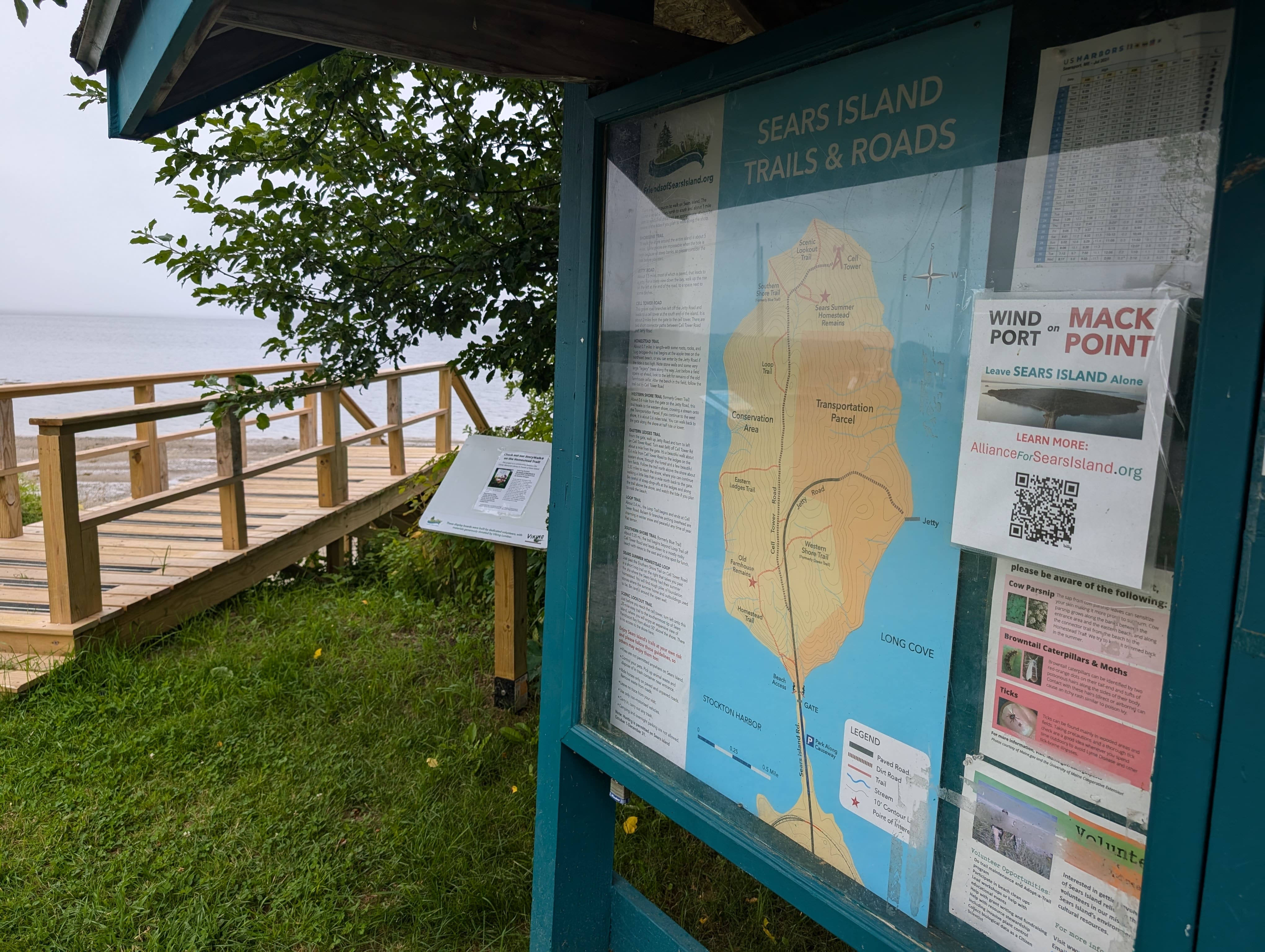 A wood pier leading to water sits next to a patch of grass with a sign showing an island map.