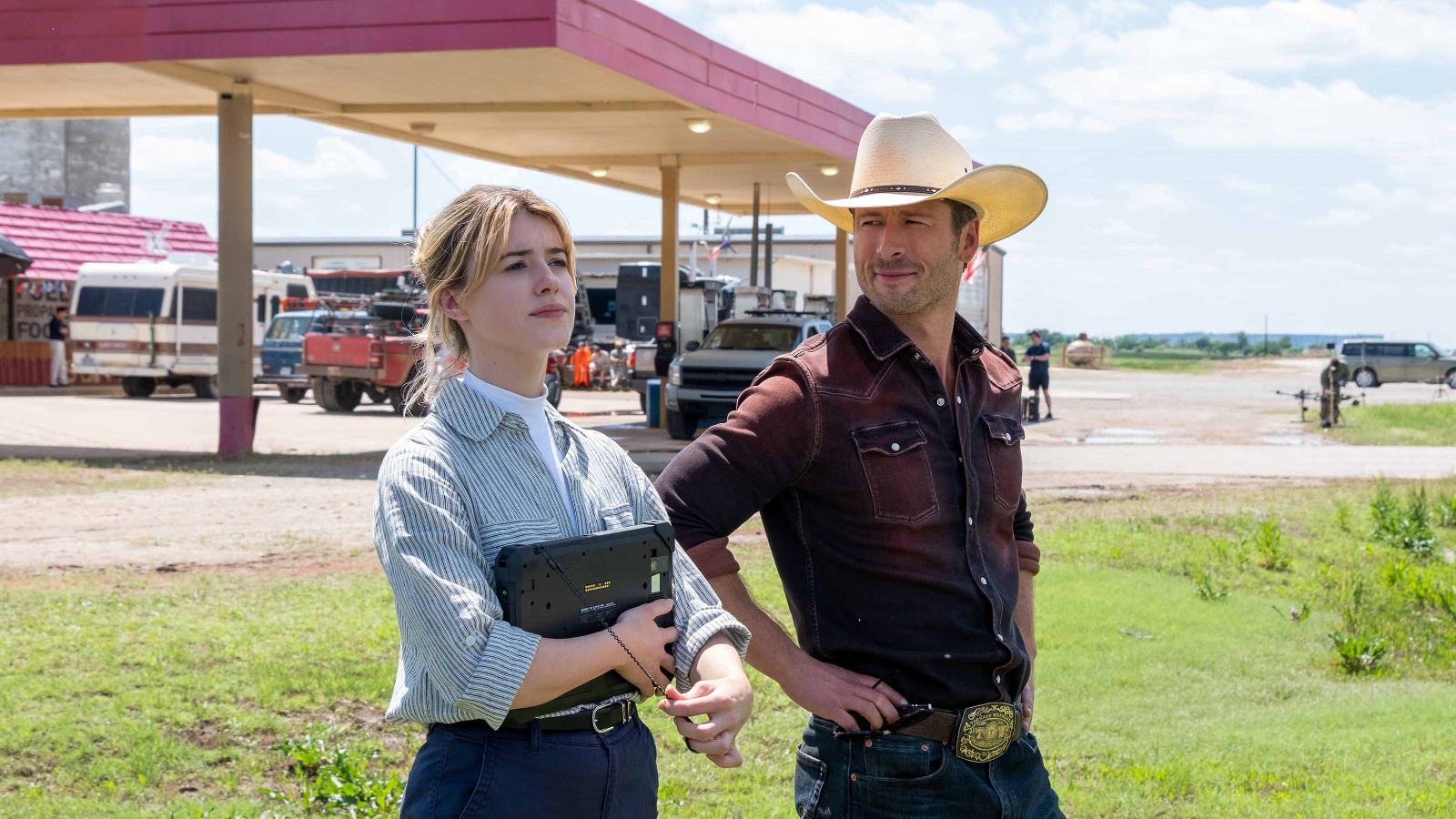 A still from the 2024 film 'Twisters' shows Glen Powell and Daisy Edgar-Jones standing in front of a gas station.