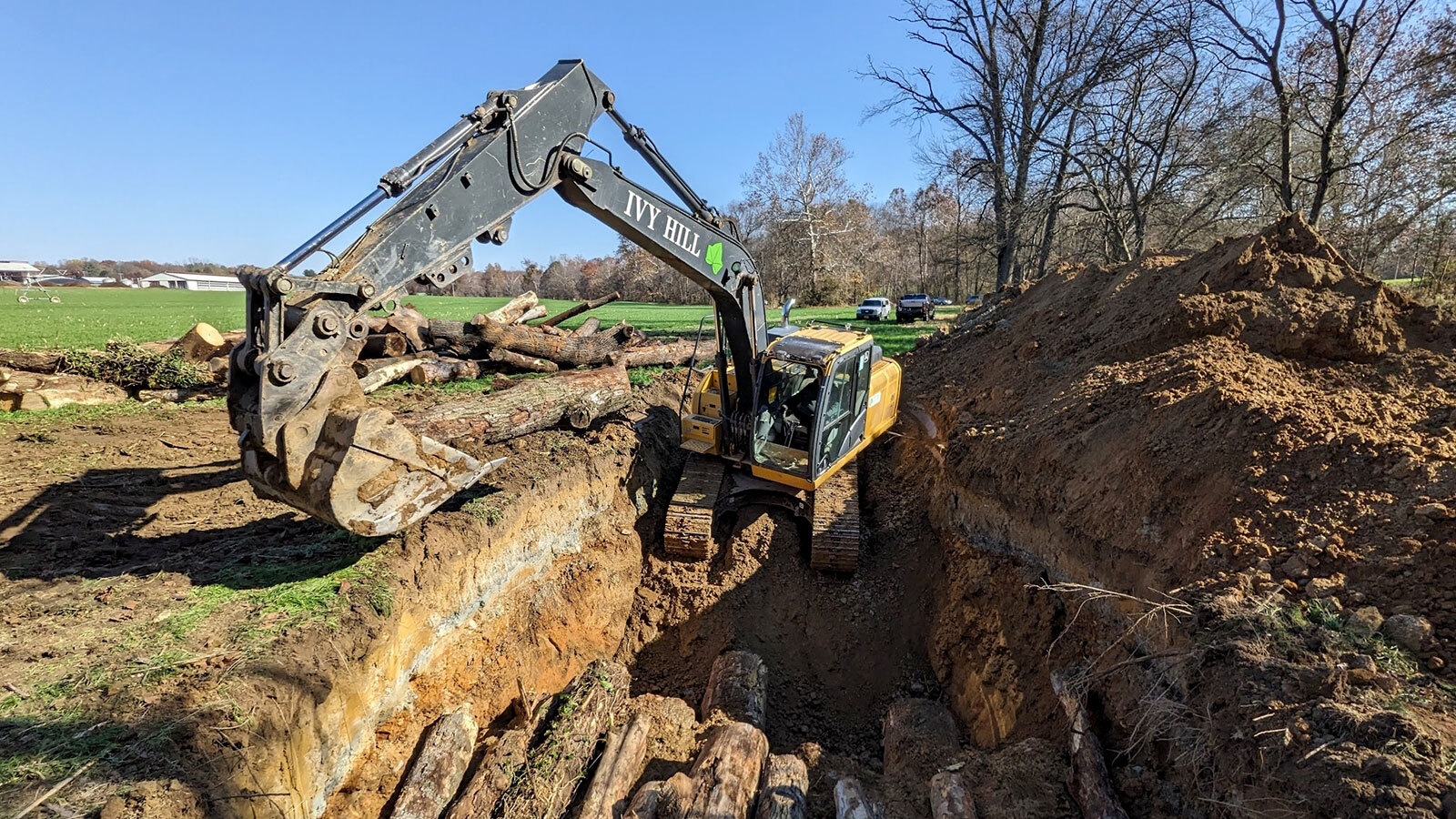 Heavy equipment buries tree logs in a freshly dug vault in a field