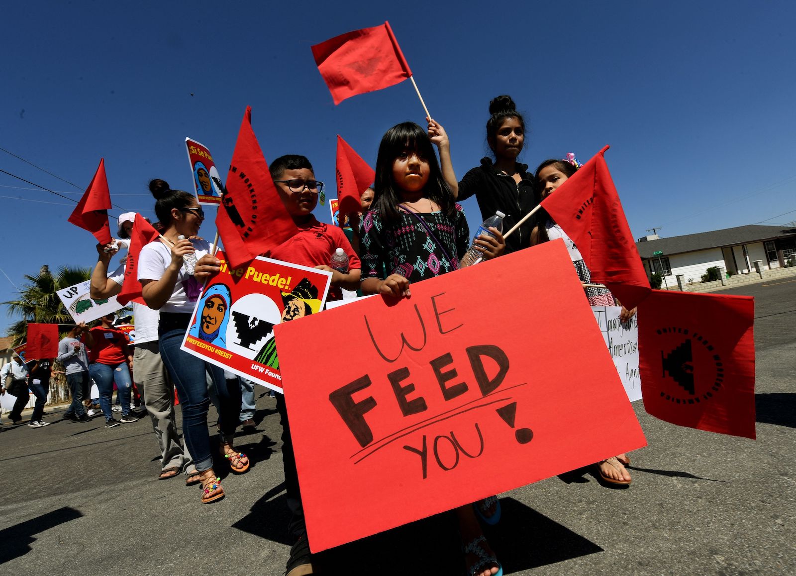 A young girl carries a red sign that says 'We FEED You'