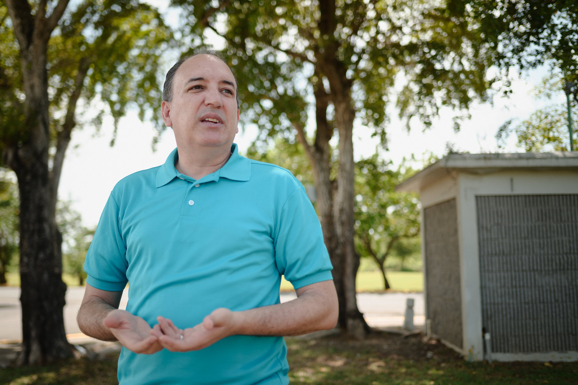 A man in a teal shirt stands near trees