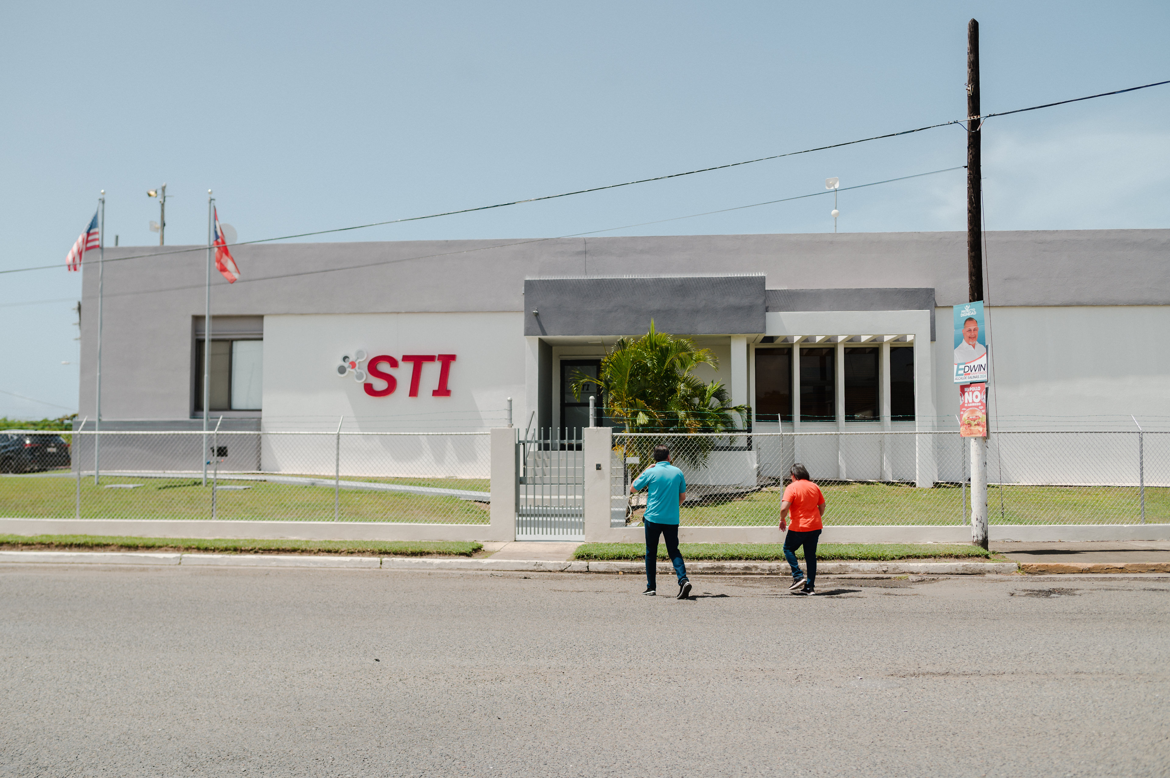 Two people stand near a large building with the letters 'STI' on it