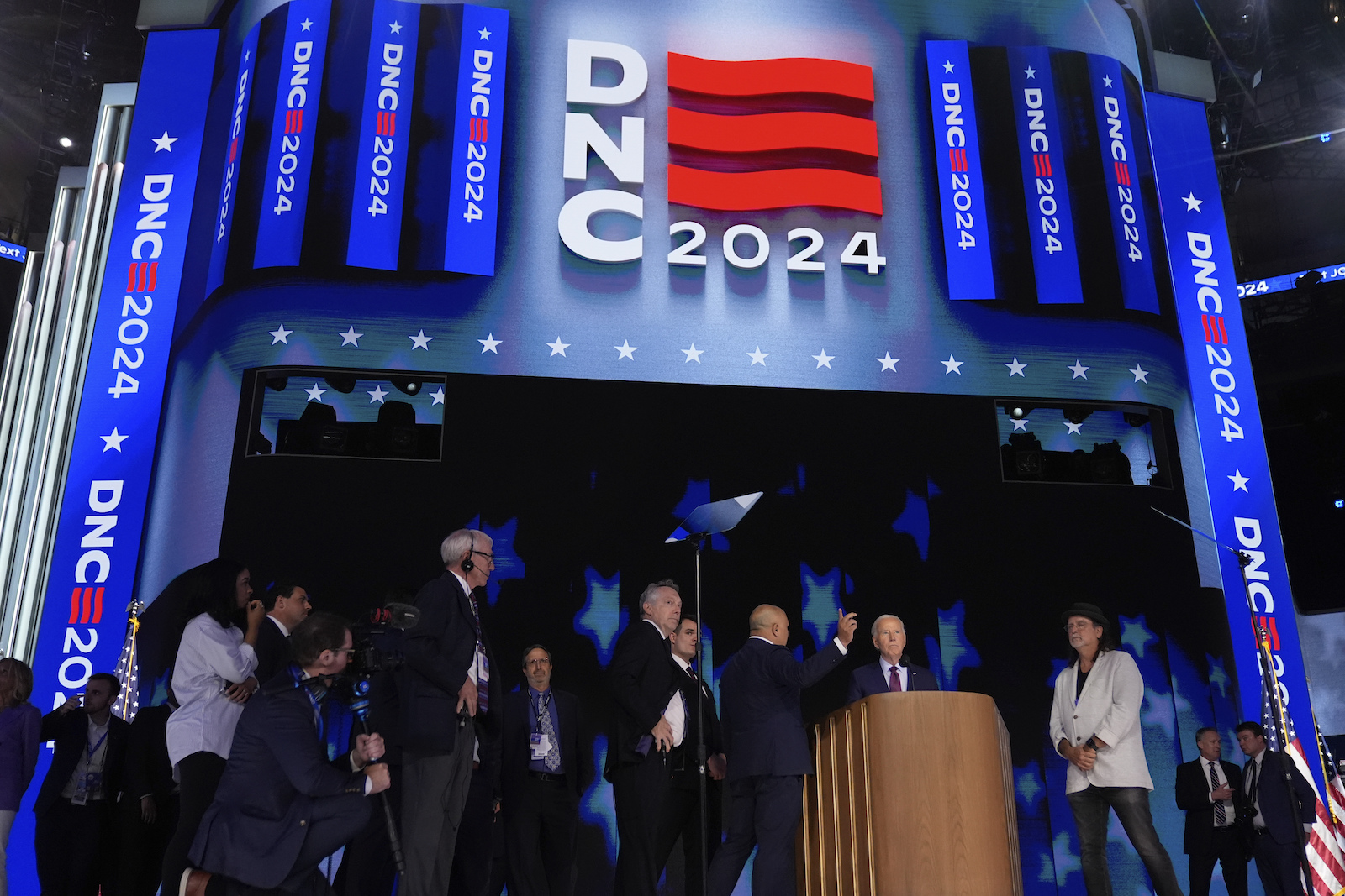 Tall marquee in blue and red and white on TV/convention stage, with wooden podium and people milling around.