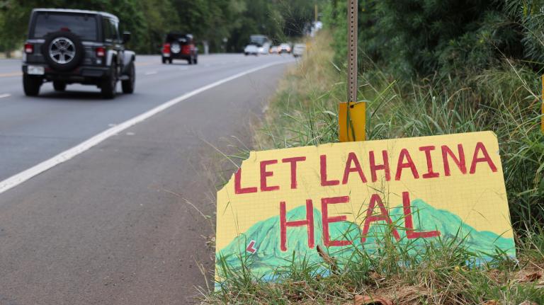 A handpainted sign in yellow, red and green reads "Let Lahaina HEAL."