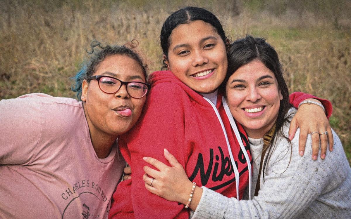 A woman and two teenage girls hug each other and smile for the camera