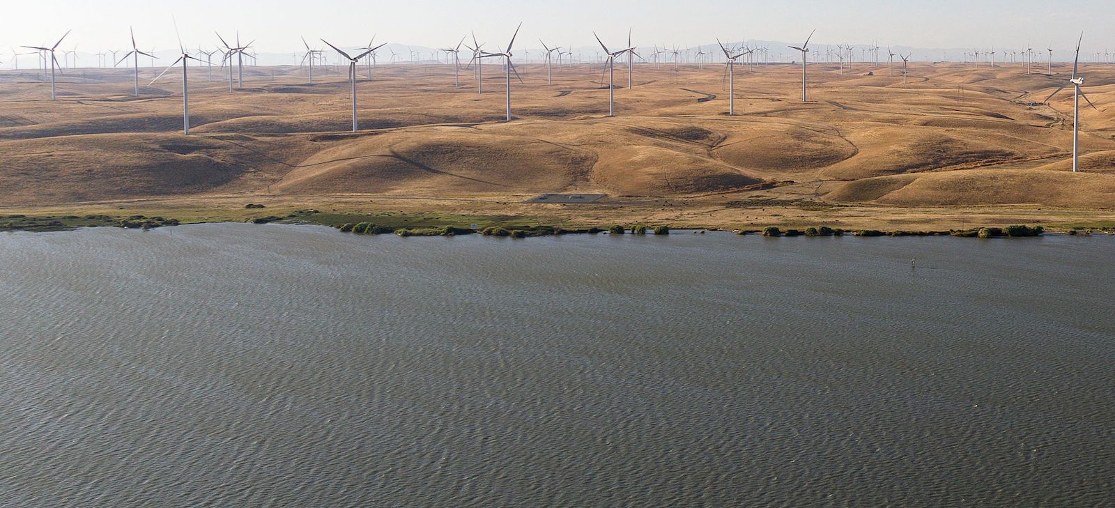 Aerial photo of river near golden hills and wind turbines