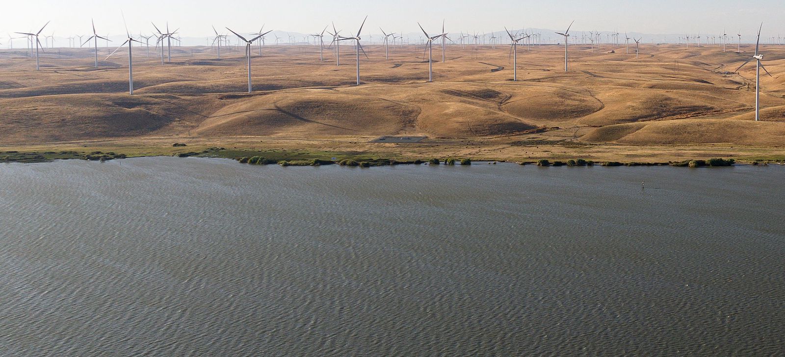 Aerial view of river near golden hills and wind turbines