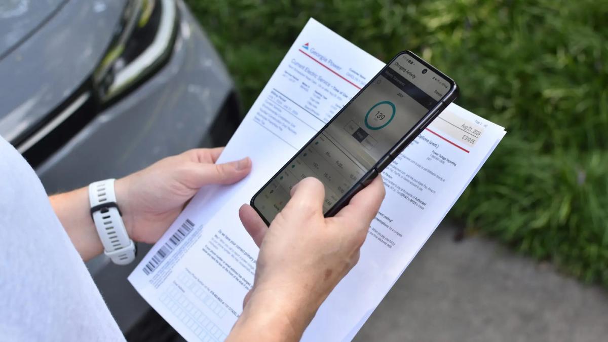 A woman holds a phone and a power bill looking at a usage graphic