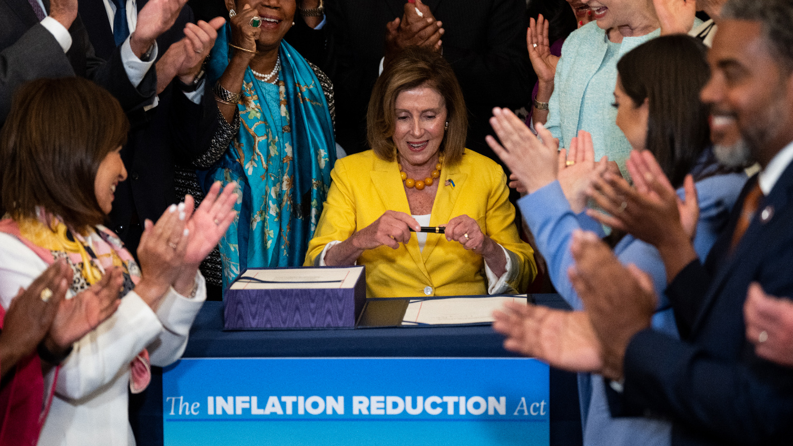 Photo of Nancy Pelosi signing a bill as people around her applaud