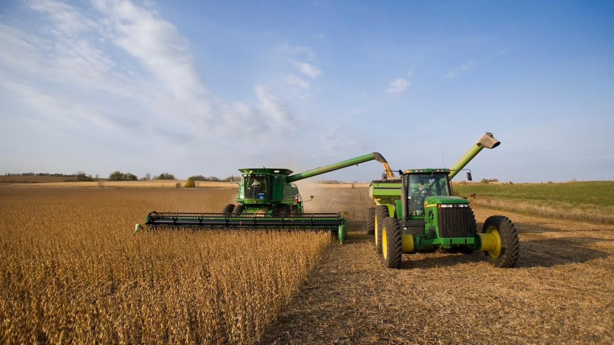 Frontal view of a large piece of John Deere farming equipment harvesting a field of soybeans
