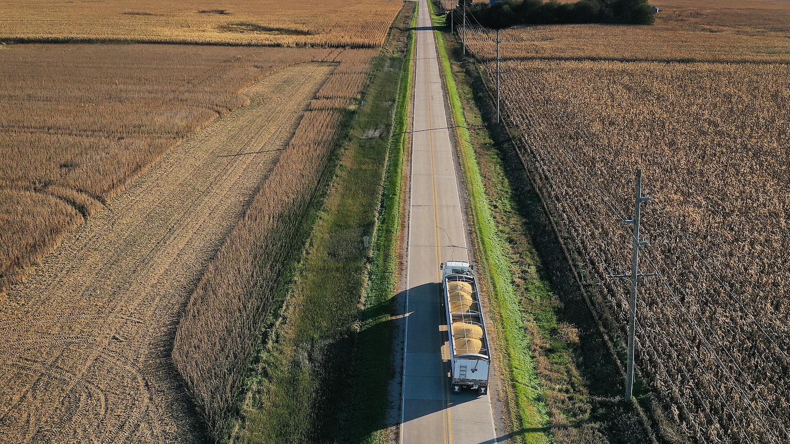 Aerial view of a large truck transporting two large containers of soybeans on a two-lane country road with farmland on either side