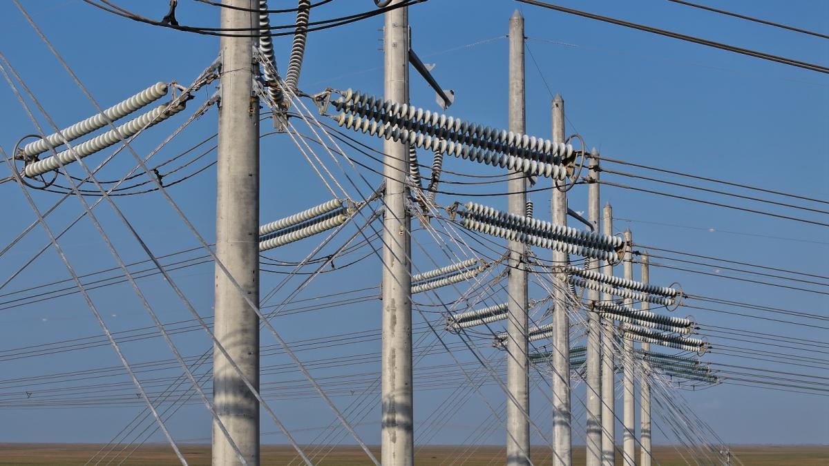 A series of power lines stand against a blue sky.