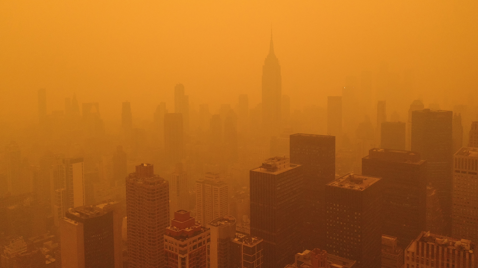 the silhouettes of sky scrapers are barely visible against an orange background of smoky sky