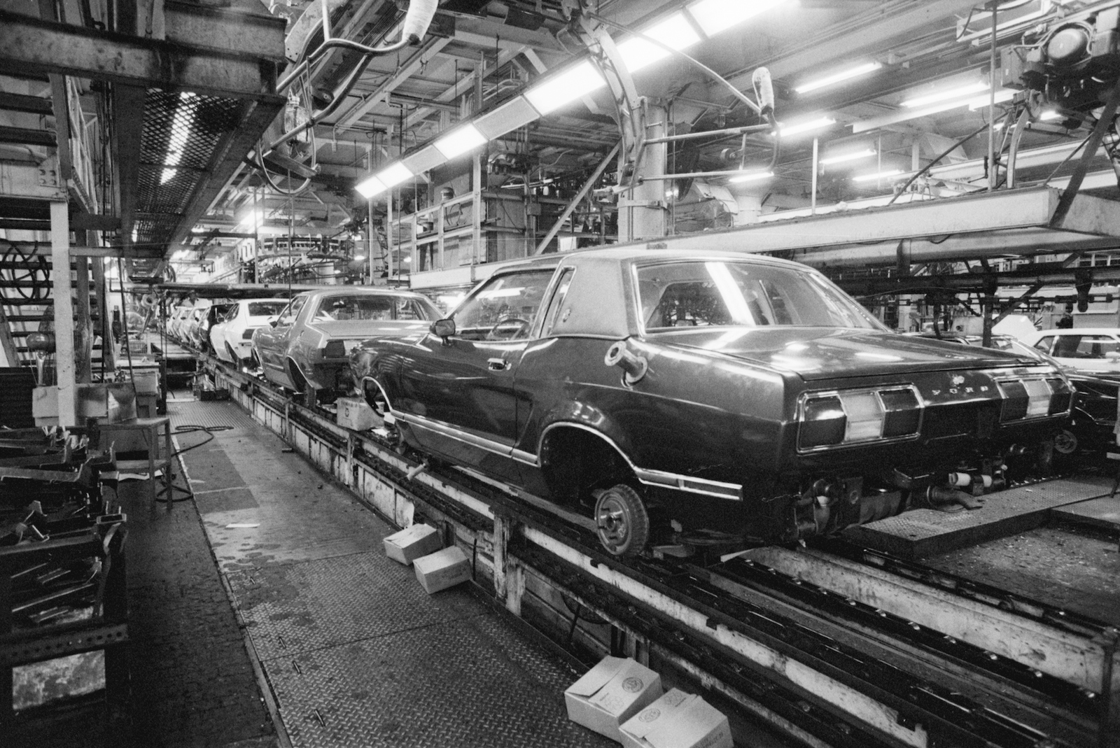 A car sits on an assembly line without workers in a black and white photo