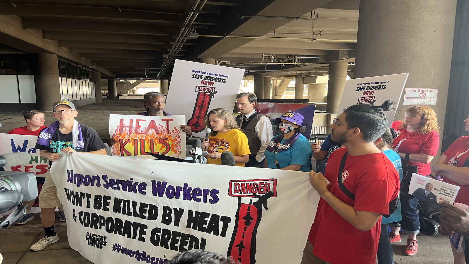 A group of people gather at an airport and hold up signs