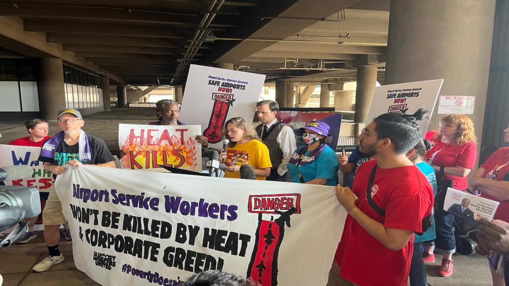 A group of people rally at an airport, holding up signs