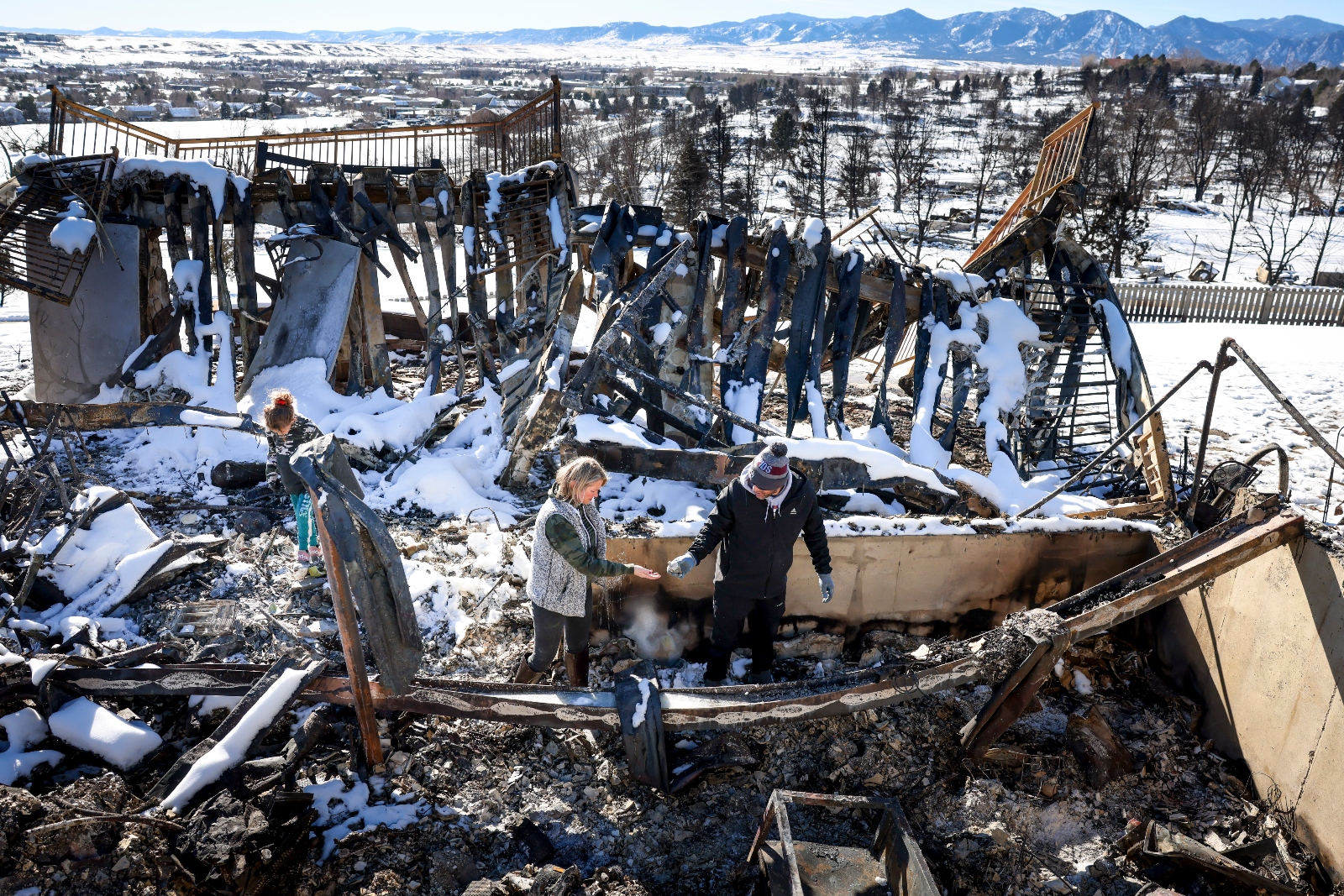 A man, woman, and child sort through the charred remains of their house after a wildfire destroyed it