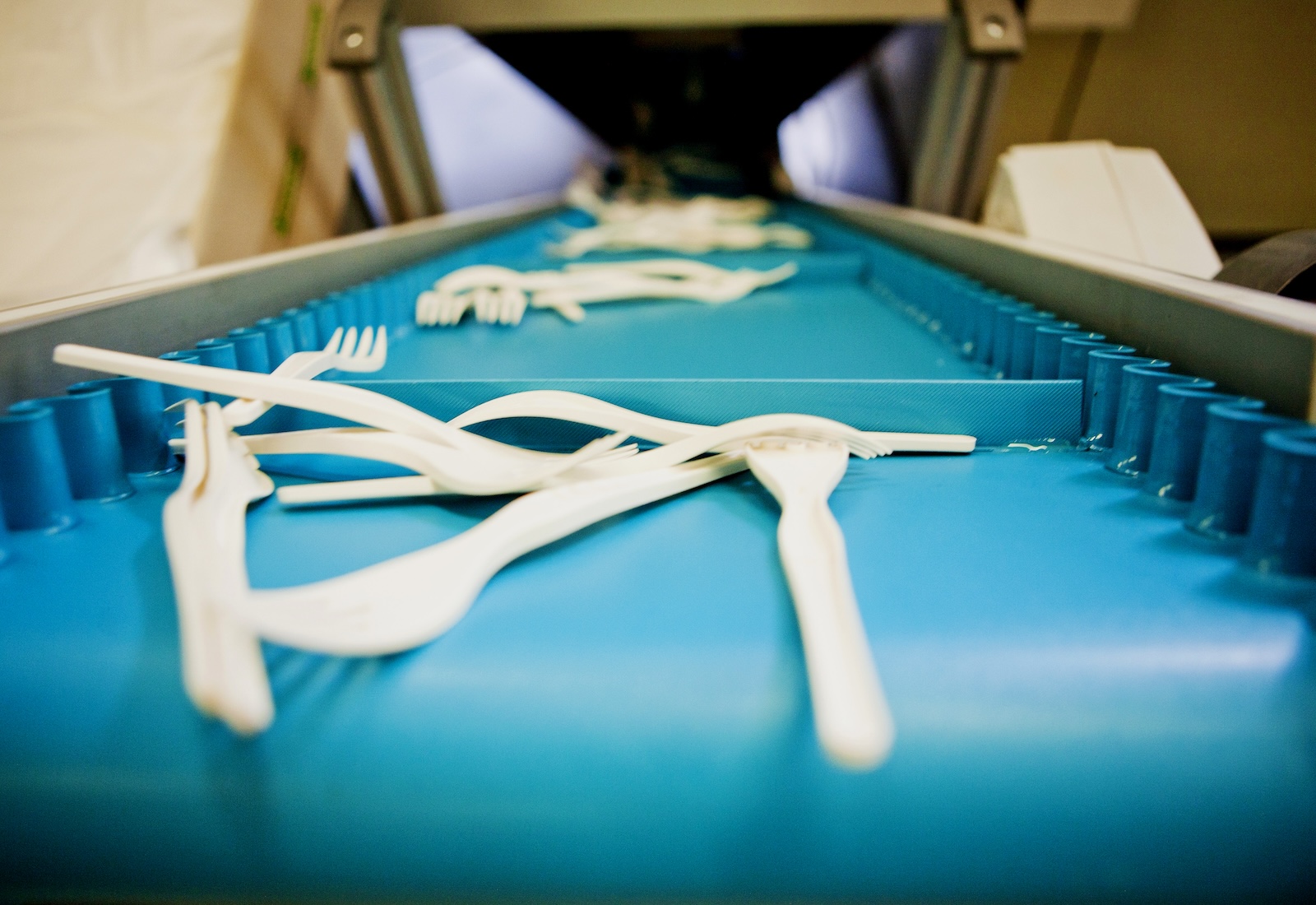 Composable cutlery moves along a blue conveyor belt away from the camera.