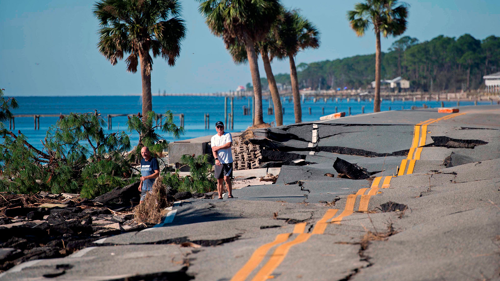 Two men stand on the side of a road that was destroyed during Hurricane Michael