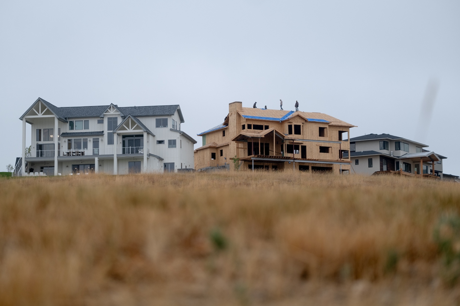 Three palatial homes, the one in the middle is still under construction and a group of workers stand on its roof