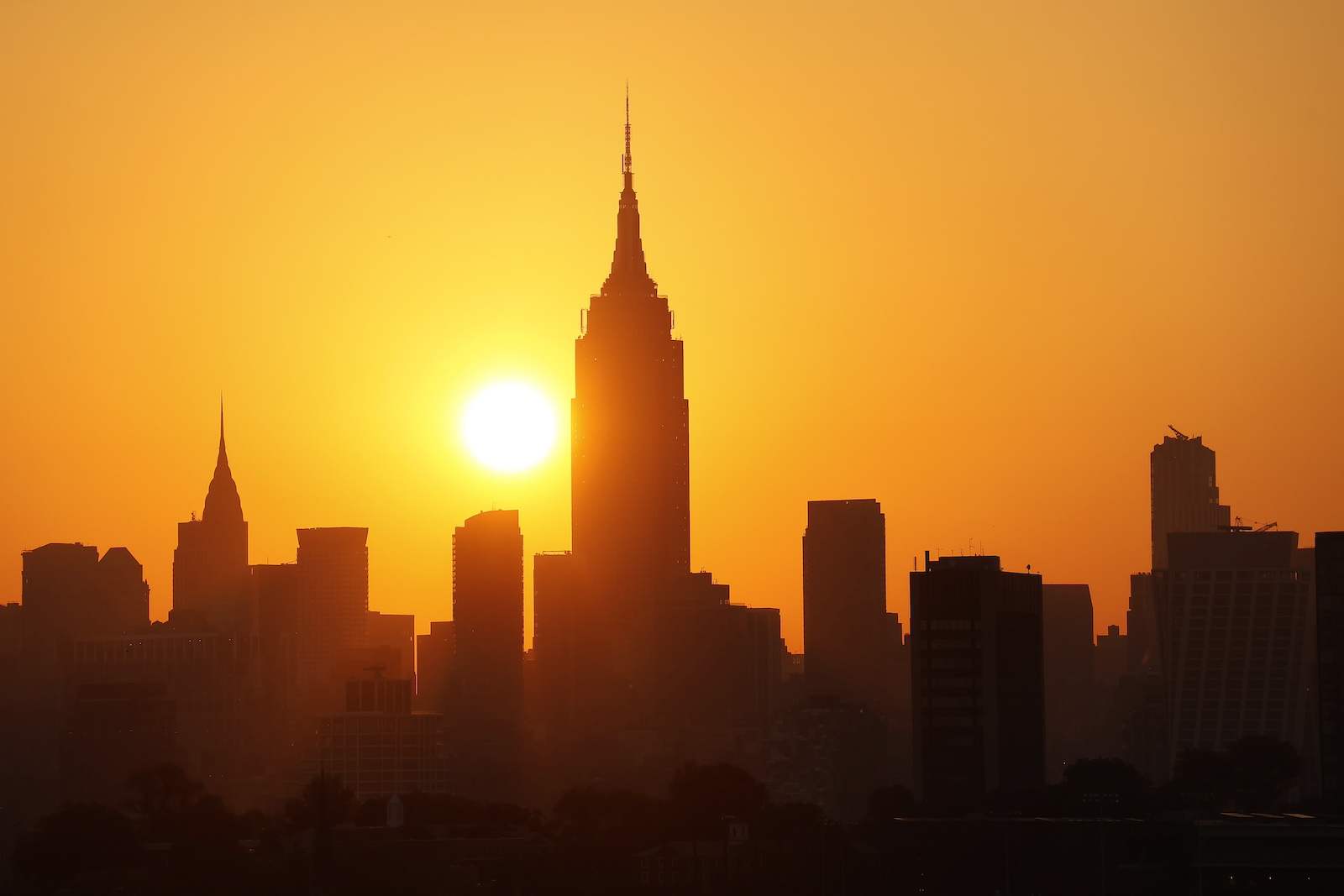 ’n Geel son kom op teen ’n donker skyline van New York, met die Empire State-gebou in die middel