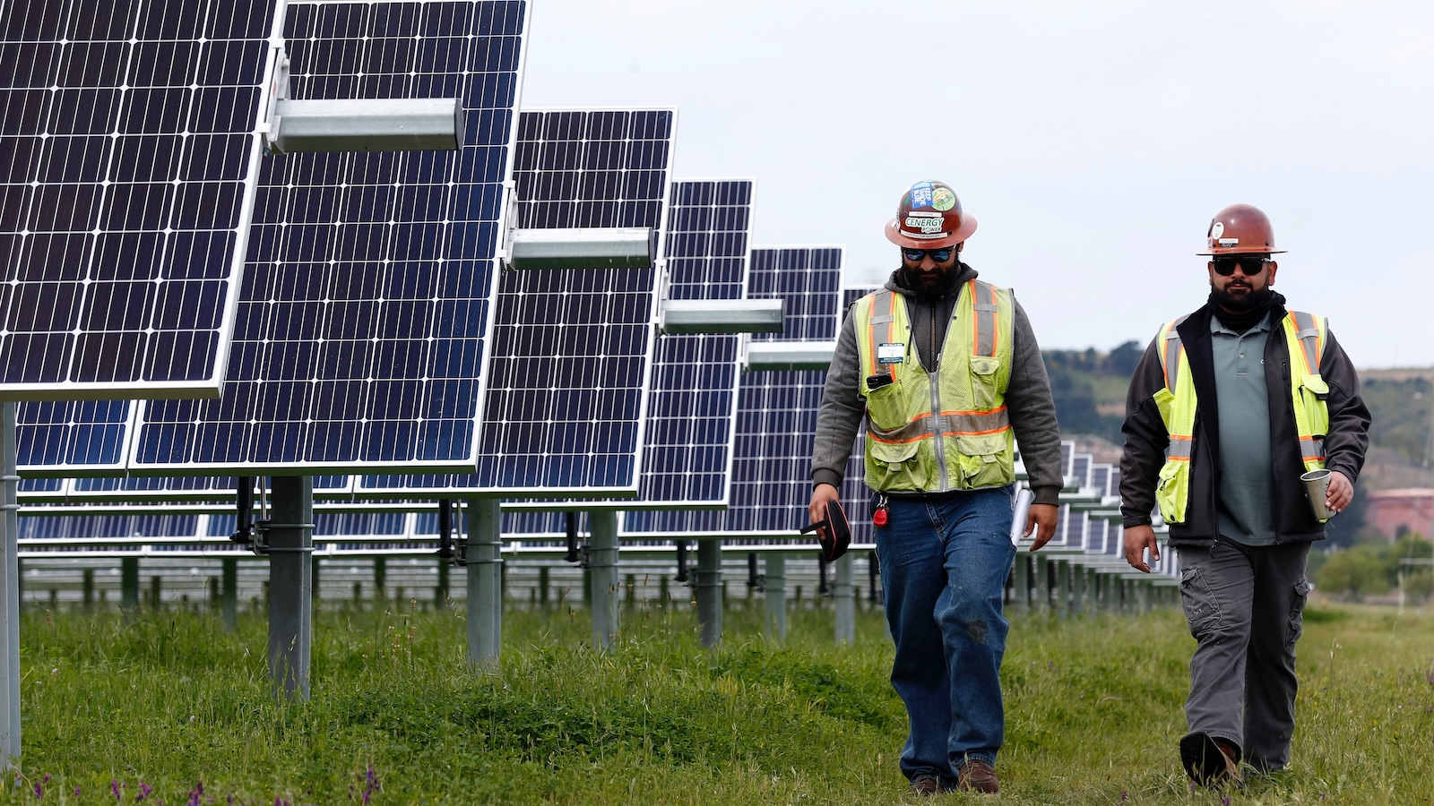 two construction workers walk through a field of solar arrays erected outside the Chevron refinery in Richmond, California.