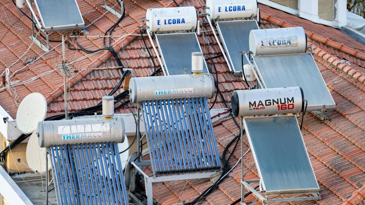 A red tile roof is covered by solar panels and heat tanks and snaking cables