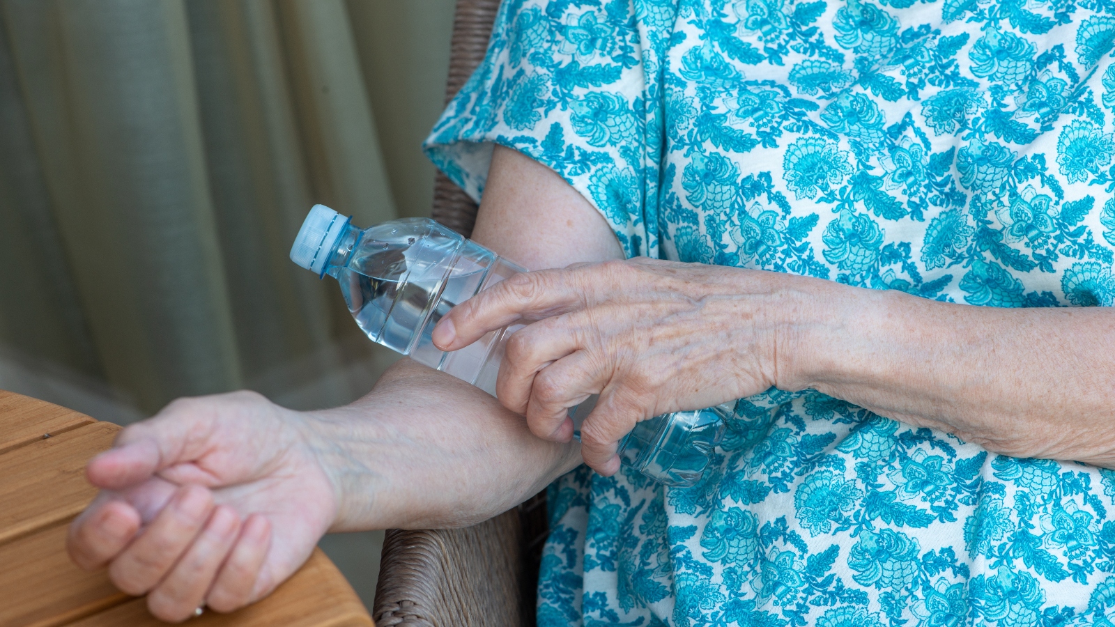 A woman in a blue shirt holds a cold water bottle to her arm