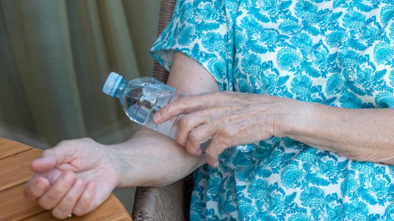 A woman in a blue shirt holds a cold water bottle to her arm